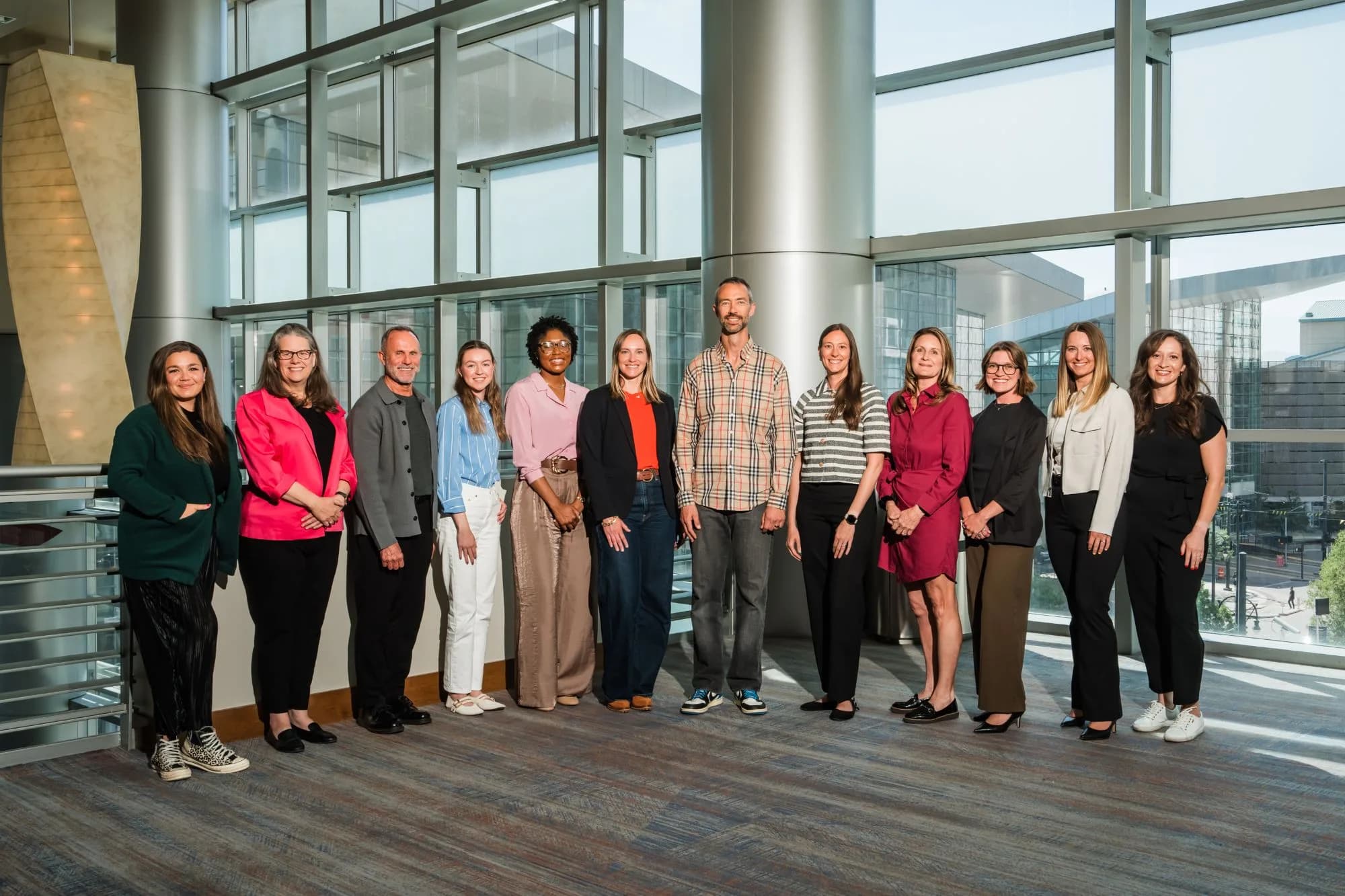 The Steadman Group team: twelve colleagues standing in a row in a sunlit atrium in front of floor-to-ceiling windows